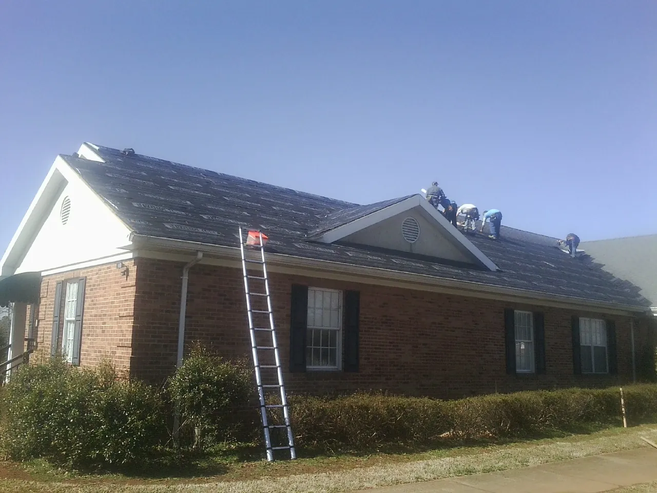 Crew tearing shingles off a brick ranch roof with a ladder set — Emergency Roof Repair work by our crew in Dahlonega