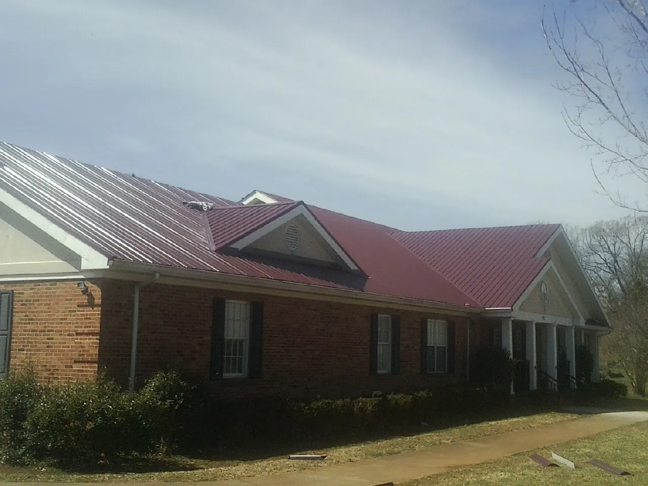 Red metal roof with gabled entries on a long brick building, from a Hail Damage Roof Repair job in Dahlonega