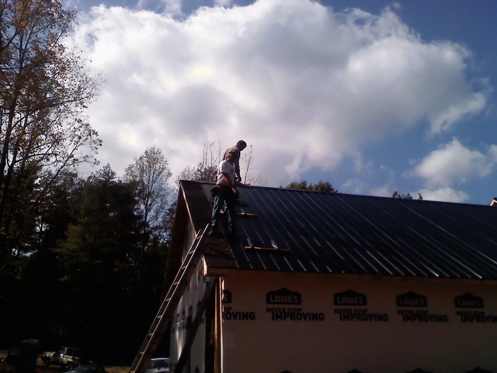 Roofer fastening dark metal panels high against a cloudy sky, from a Roof Inspection job in Dahlonega