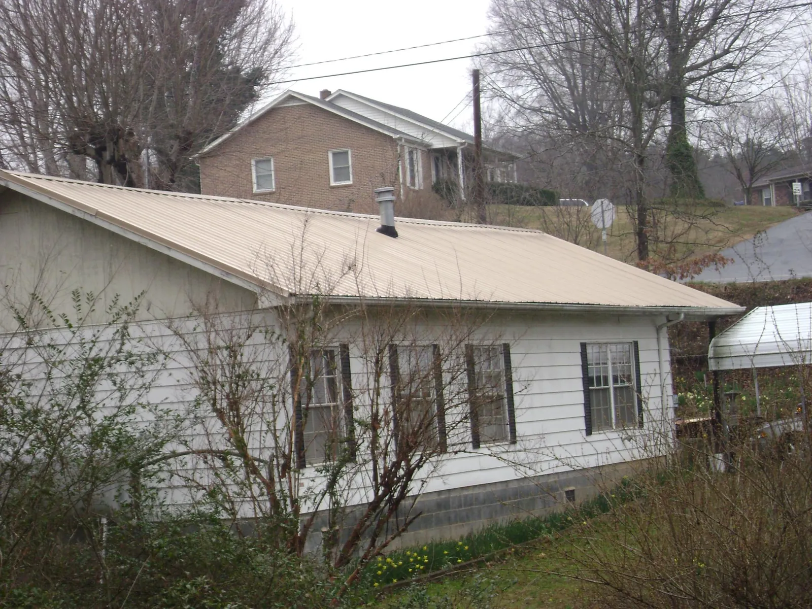Tan metal roof on a white sided house set into a hillside — Commercial Roofing by Roofing Brothers in Dahlonega
